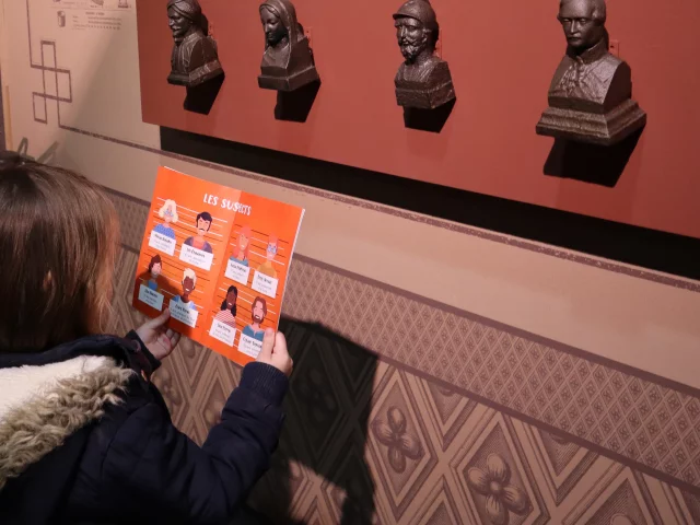 Petite fille avec une affiche dans les mains face à des sculptures accrochées au mur