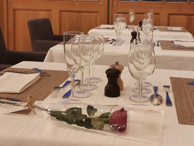 Table dressée dans un restaurant avec couverts, verres et une rose posée au premier plan