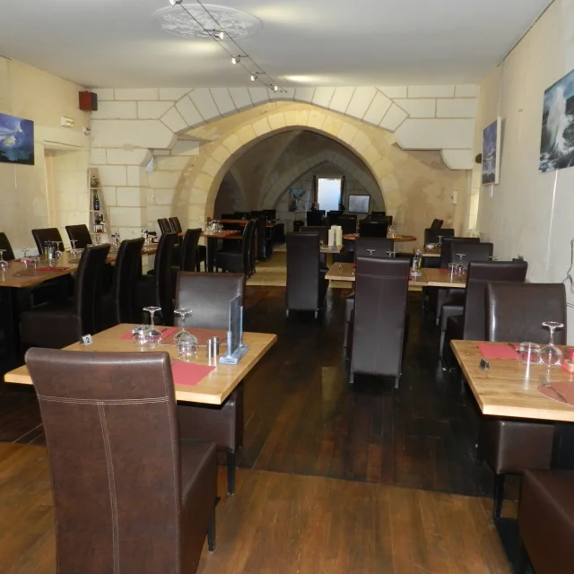 Vue sur une salle de restaurant voutée avec tables en bois et chaises en cuir marron